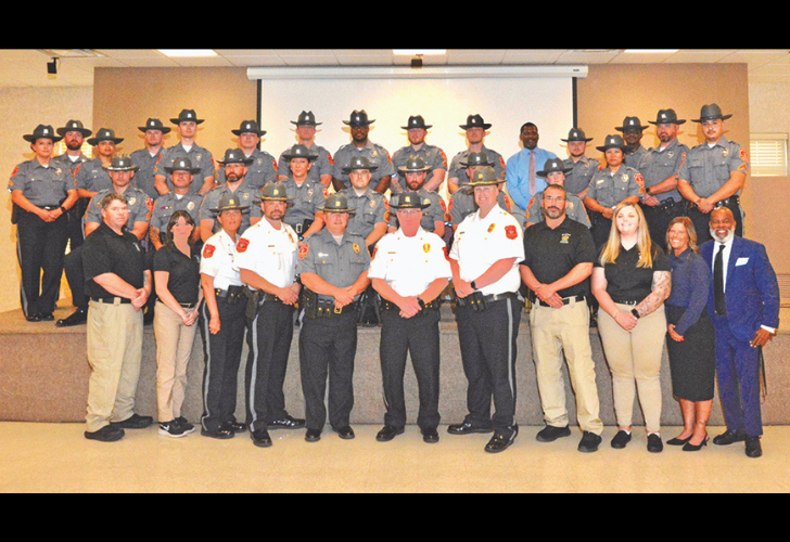 Awards Group photo of about 30 law enforcement officers in uniform, posing on a stage and floor with a few civilians in front, in a training room.