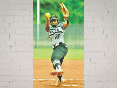 Female softball pitcher in a Braves uniform mid-pitch on the infield, glove up, sunny field in the background.