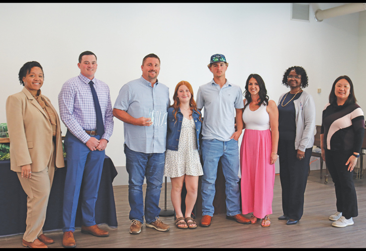 Eight adults of diverse ages and backgrounds posing in a bright room for a group photo.