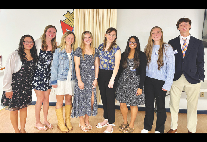 Nine students posing together in a hall, smiling at the camera, wearing casual outfits and name tags.