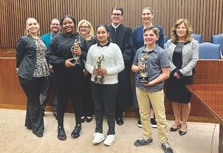 Group of diverse award recipients posing with trophies in a formal room, smiling for the photo after a ceremony.
