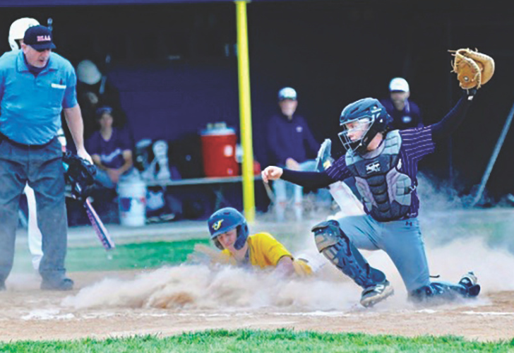 Baseball scene: a catcher in blue gear reaches to tag a sliding baserunner in a yellow shirt as dust kicks up near home plate, with an umpire watching on the left.