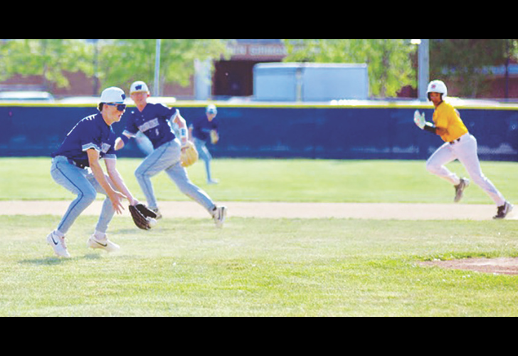 McCabe S25 Baseball game on a sunny field: three infielders in blue uniforms reach for a ground ball as a runner in yellow races forward on the right.