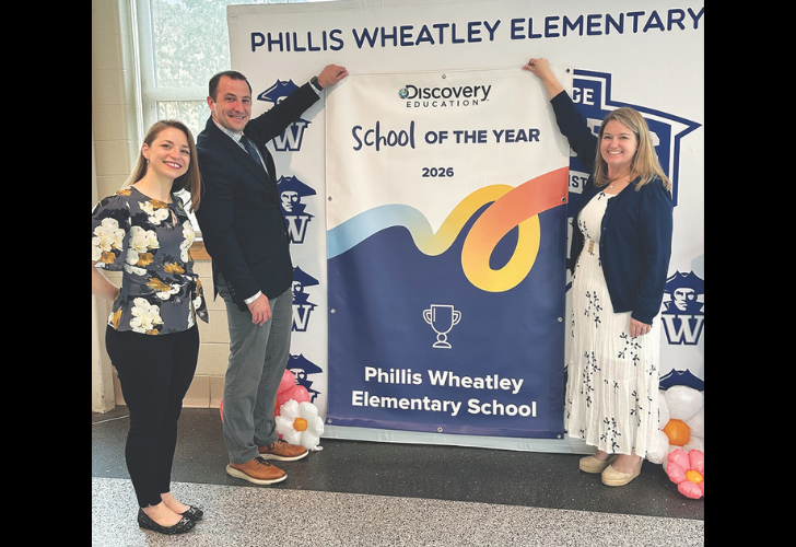 Three adults pose with a 'School of the Year 2026' banner at Phillis Wheatley Elementary School, celebrating the award.