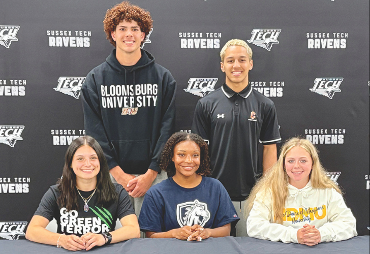 Five students posing for a photo at a school event, three seated at a table and two standing behind them, backdrop reads Sussex Tech Ravens.