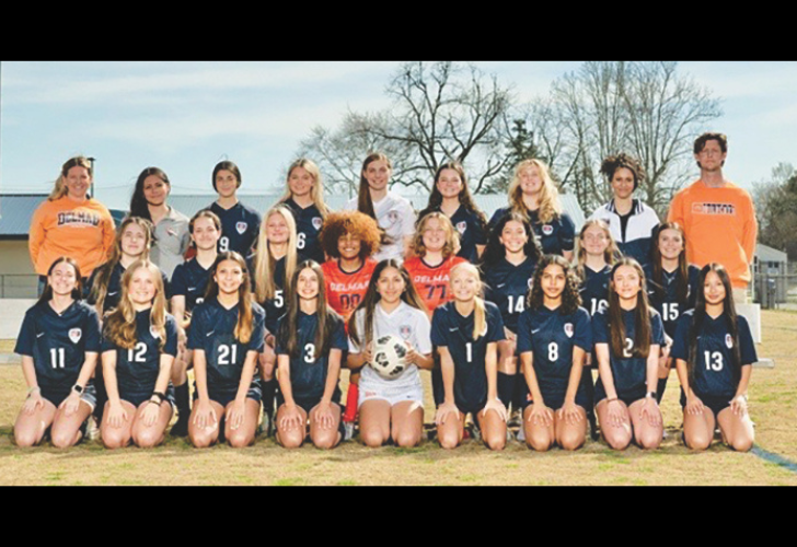 Girls soccer team group photo on a field, players in navy uniforms, center player holds a soccer ball.