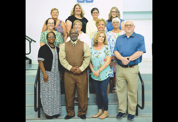 Faculty- page 6 Group of twelve diverse adults posing on a stairway for a team photo, smiling at the camera.