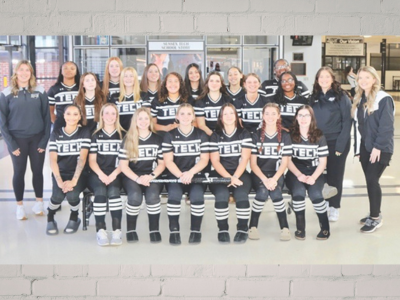 Large group portrait of people wearing matching black T-shirts with white lettering, posing indoors for a team photo.