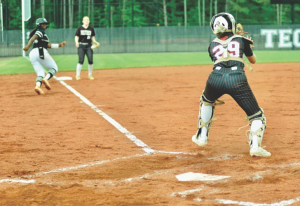 Catcher at home plate ready to tag as a baserunner slides in during a softball game on a dirt field.