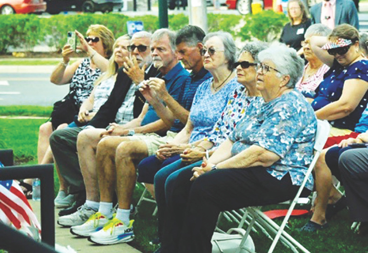 CROWD - time capsule audience Group of seniors seated on folding chairs at an outdoor event, some wearing sunglasses; a spectator is taking a photo.