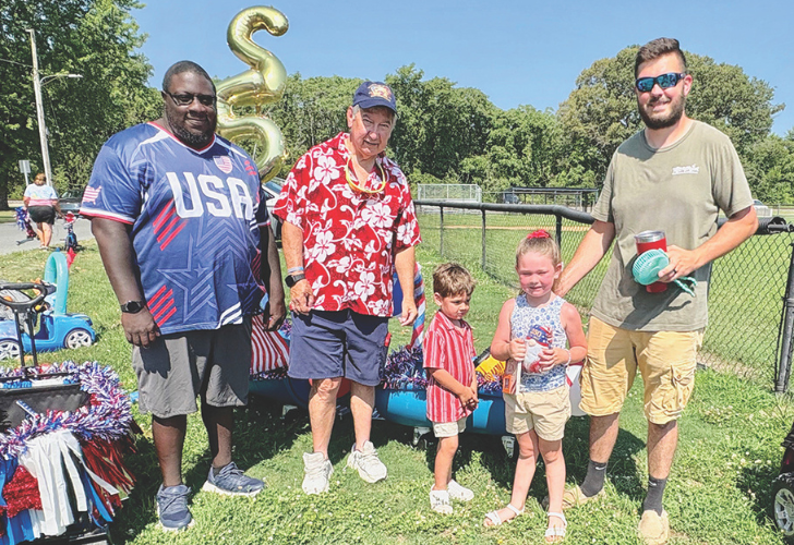 Delaware 4 Group of five people at a sunny park event, including two children, a man in a USA jersey, an older man in a red Hawaiian shirt, and a man with a drink, near patriotic decorations.