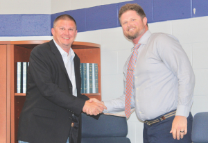 Delmar School Board Two men in business attire shake hands in an office setting beside a bookshelf with binders behind them.