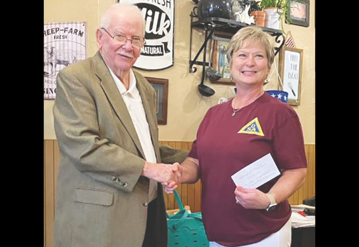 Donation Blackwell Elderly man in a beige blazer shakes hands with a smiling woman in a maroon shirt, holding a card, during a small indoor event.