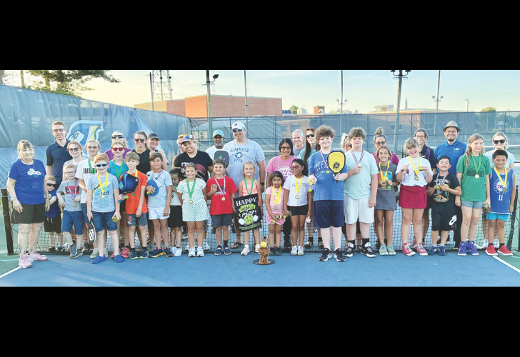 PICKLEBALL 38 Group of children and coaches on a tennis court posing for a photo with medals after a tournament.
