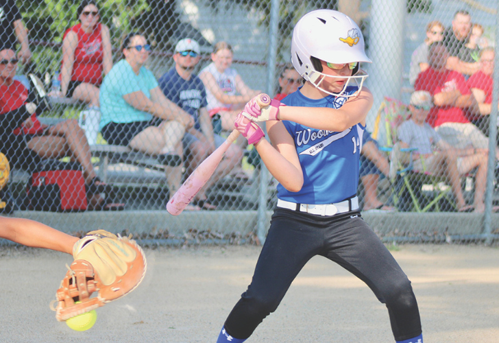 ROMER 37 Young girl in a blue softball uniform batting, wearing a helmet and pink gloves, with a catcher and crowd in the background.