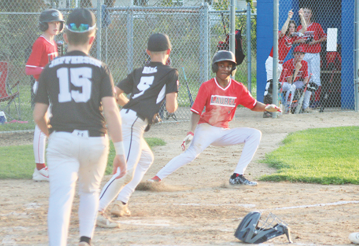 RUNDOWN2 39 Youth baseball game: a runner in a red Laurel jersey slides toward a base as fielders in black jerseys converge nearby.