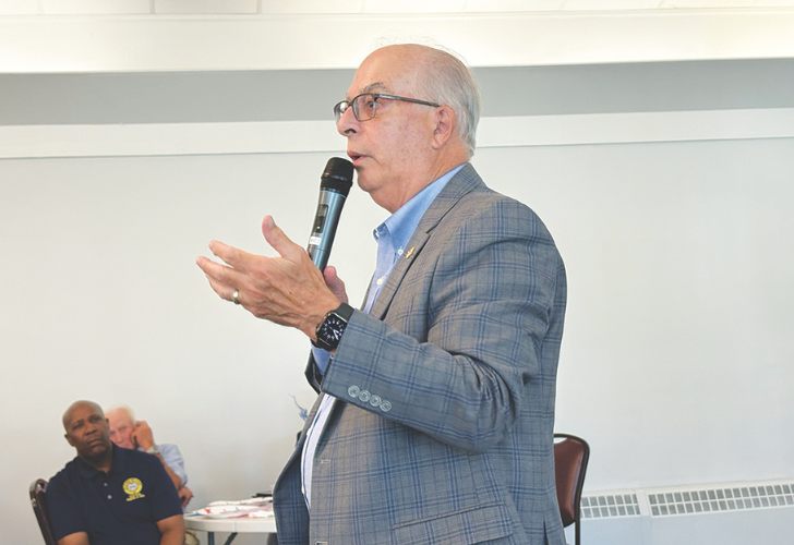 Rep. Danny Short, - page 34 Older man in a blue checked blazer speaks into a handheld microphone at a meeting, gesturing with his hands.