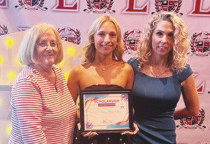 Scholarships1 6 Three smiling women pose at an awards event; center woman holds a framed certificate, with a pink backdrop and logos in the background.