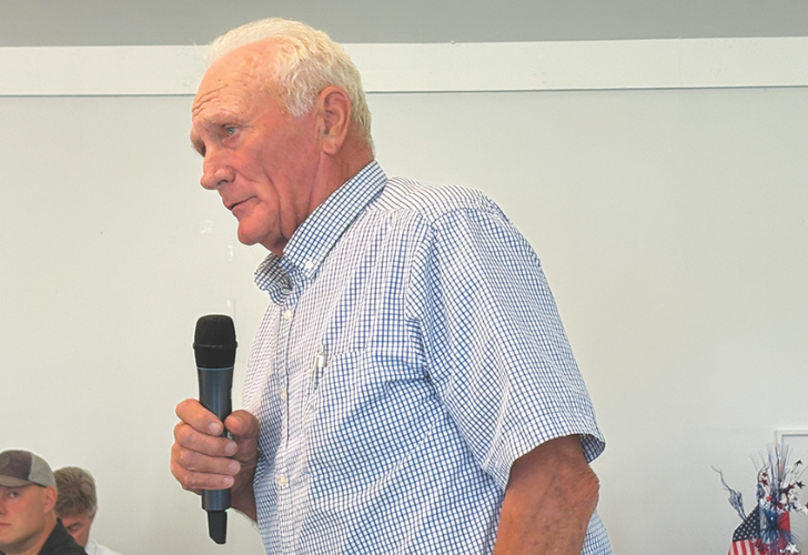 Sen. Dave Wilson Older man in a blue checkered shirt speaks into a handheld microphone at a meeting or event.