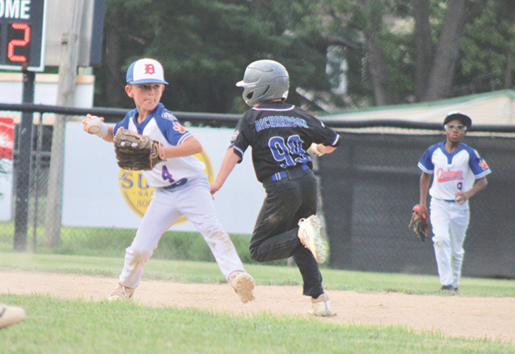 THROW TO FIRST 40 Youth baseball game: fielder in white and blue reaches toward a baserunner in a black uniform with a helmet, as a teammate stands in the background.